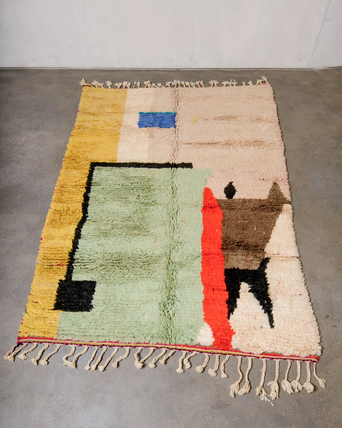 Berberlin vintage Berber rug in shades of sand, pistachio, red, yellow and blue in a modern, graphic design, laying flat on concrete studio floor.